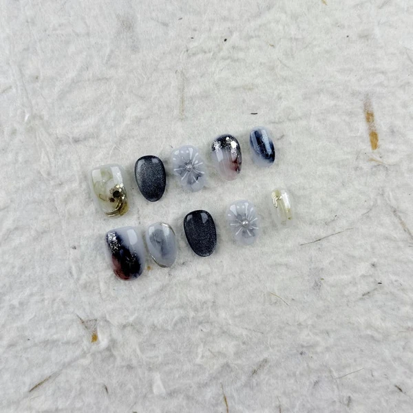 Manucure artistique courte ovale à presser en transparent, noir dégradé avec fleurs, centre de perles et effets ombrés, idéale pour les événements de