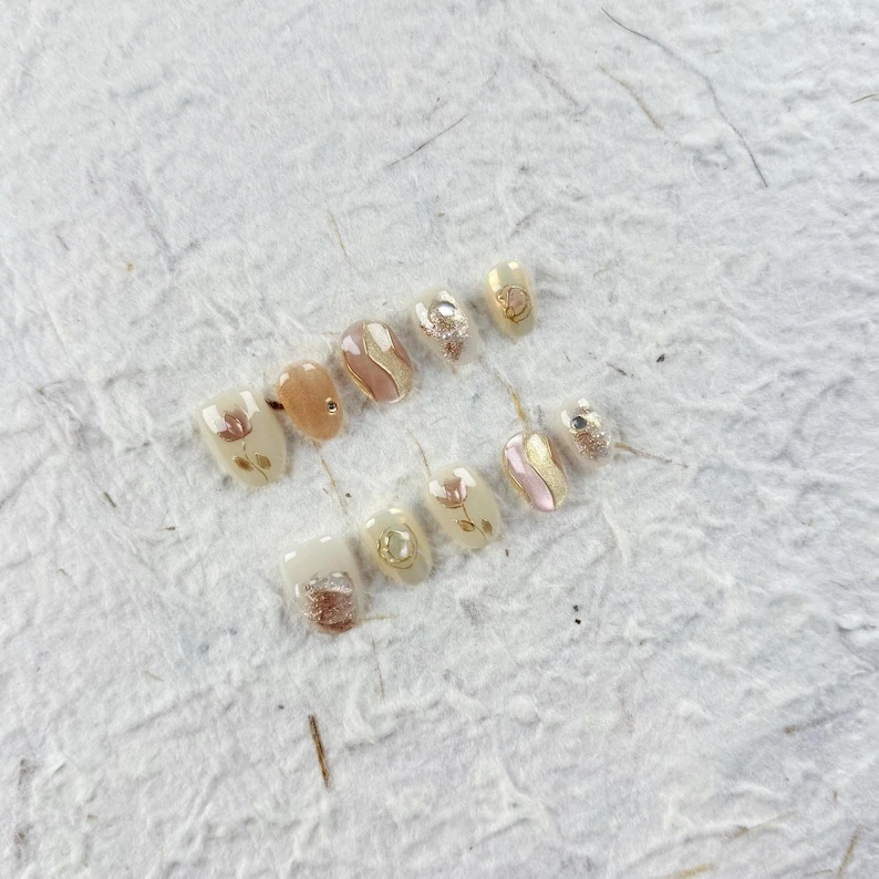 Ongles à presser ovales courts élégants en nude doux avec des lignes dorées et des strass. Parfait pour un usage quotidien et les occasions sociales