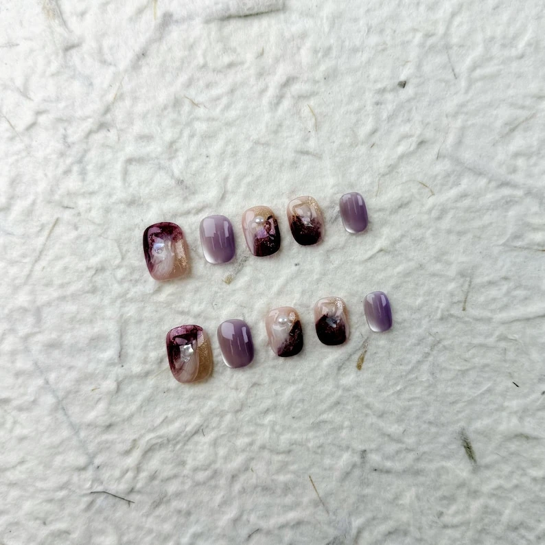 Ongles pressés carrés courts raffinés en rose nude et violet, ornés de perles et de strass. Parfait pour les fêtes et les occasions spéciales