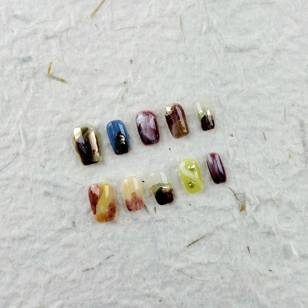 Presse carrée courte unique sur les ongles avec une texture marbrée et des dégradés de brun, bleu, violet, jaune, avec des accents métalliques