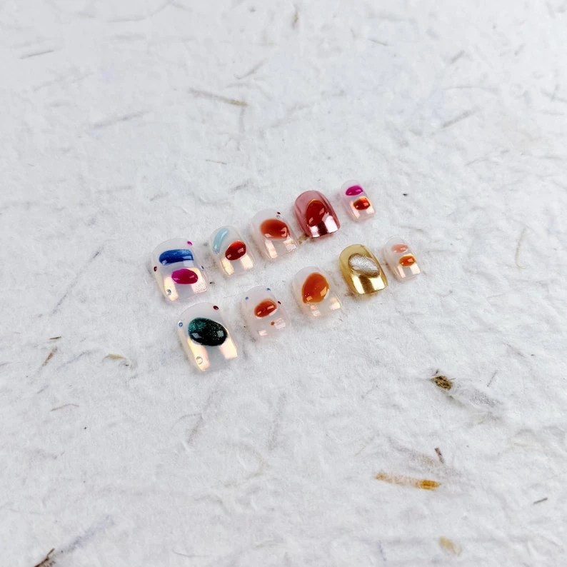 Presse carrée courte artistique sur les ongles dans une base transparente avec des blocs d'aquarelle rouge orange, jaune et bleu, faux ongles