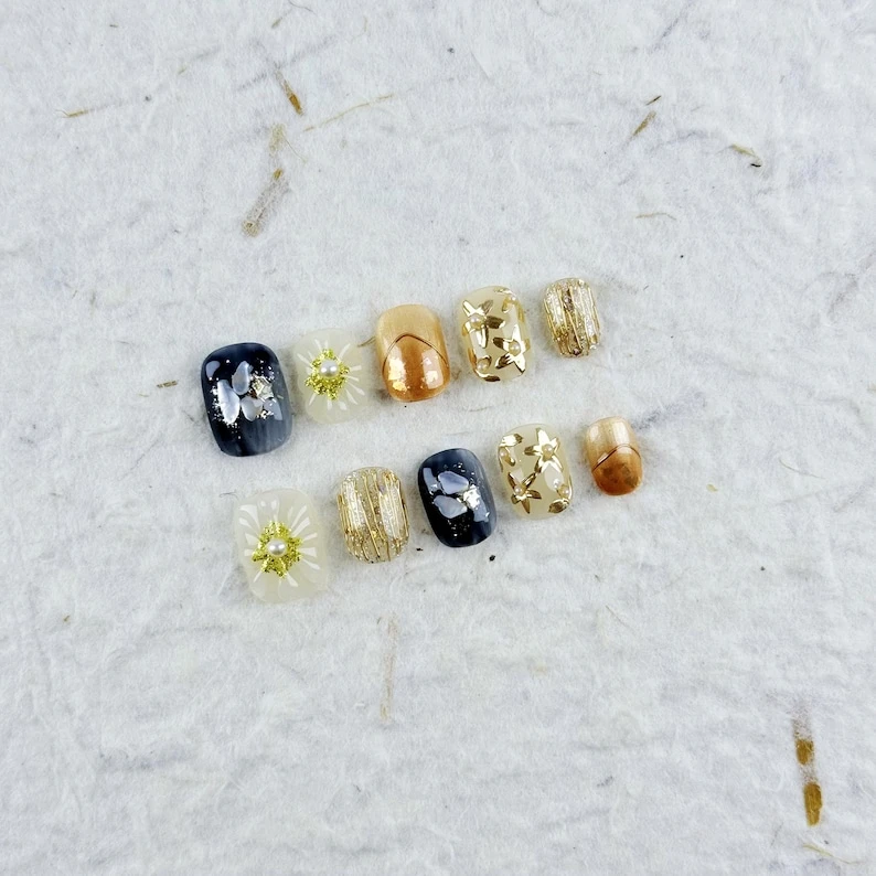 Presse-ongles carrés luxueux et courts en noir, or et cuivre avec des fleurs 3D, des perles et des accents métalliques, parfait pour les événements