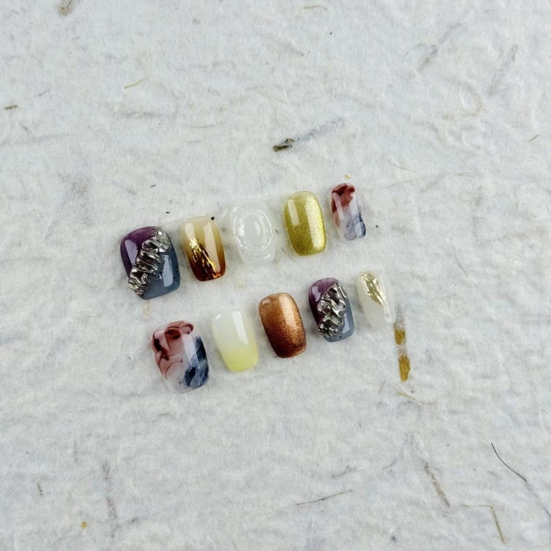 Presse carrée courte artistique sur les ongles dans des couleurs arc-en-ciel avec des accents métalliques, des motifs dégradés et un style encre,