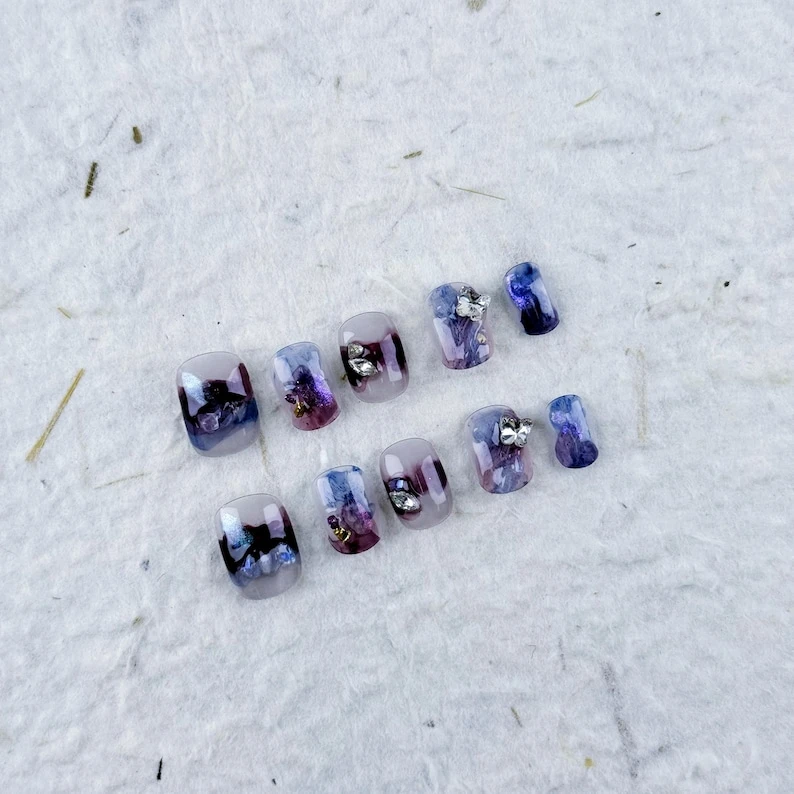Presse carrée courte sur les ongles avec dégradé violet. Papillons argentés, strass brillants pour un look mystique. Parfait pour les fêtes et les