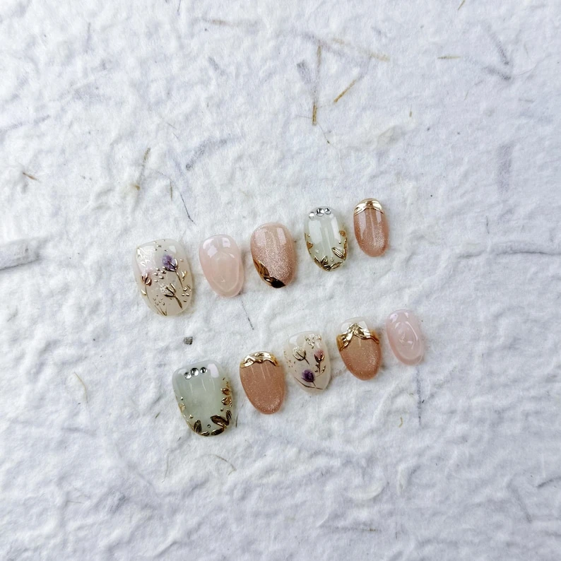 Faux ongles courts ovales rose poudré et beige, feuilles dorées, fleurs violettes, scintillement subtil, parfaits pour le quotidien et les