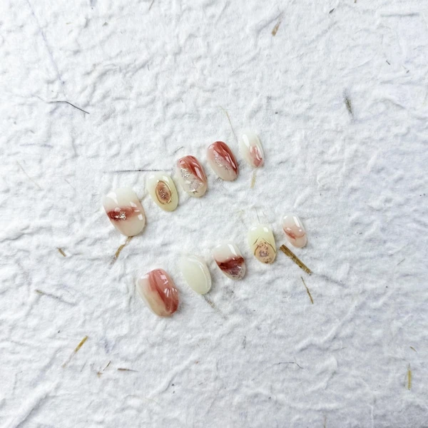 Ongles à presser ovales courts artistiques dans une base blanche avec des touches de rouge à brun ombré et d'or, parfaits pour un usage quotidien