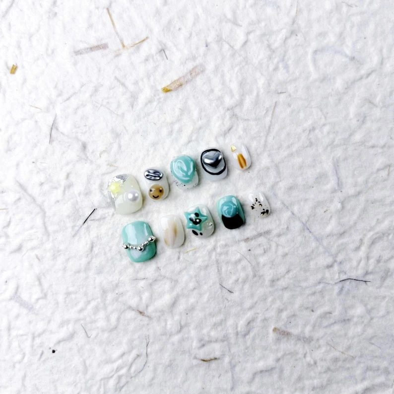 Courte pression ovale sur les ongles en bleu pastel avec des perles, des étoiles, des smileys et des images de chat, de jolis faux ongles pour les