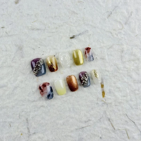 Presse carrée courte artistique sur les ongles dans des couleurs arc-en-ciel avec des accents métalliques, des motifs dégradés et un style encre,