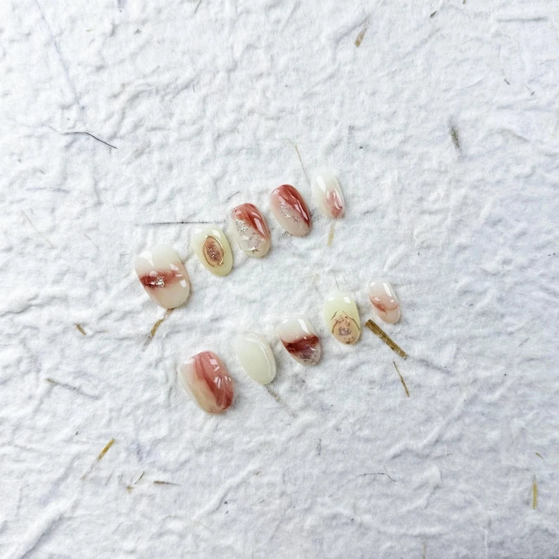 Ongles à presser ovales courts artistiques dans une base blanche avec des touches de rouge à brun ombré et d'or, parfaits pour un usage quotidien